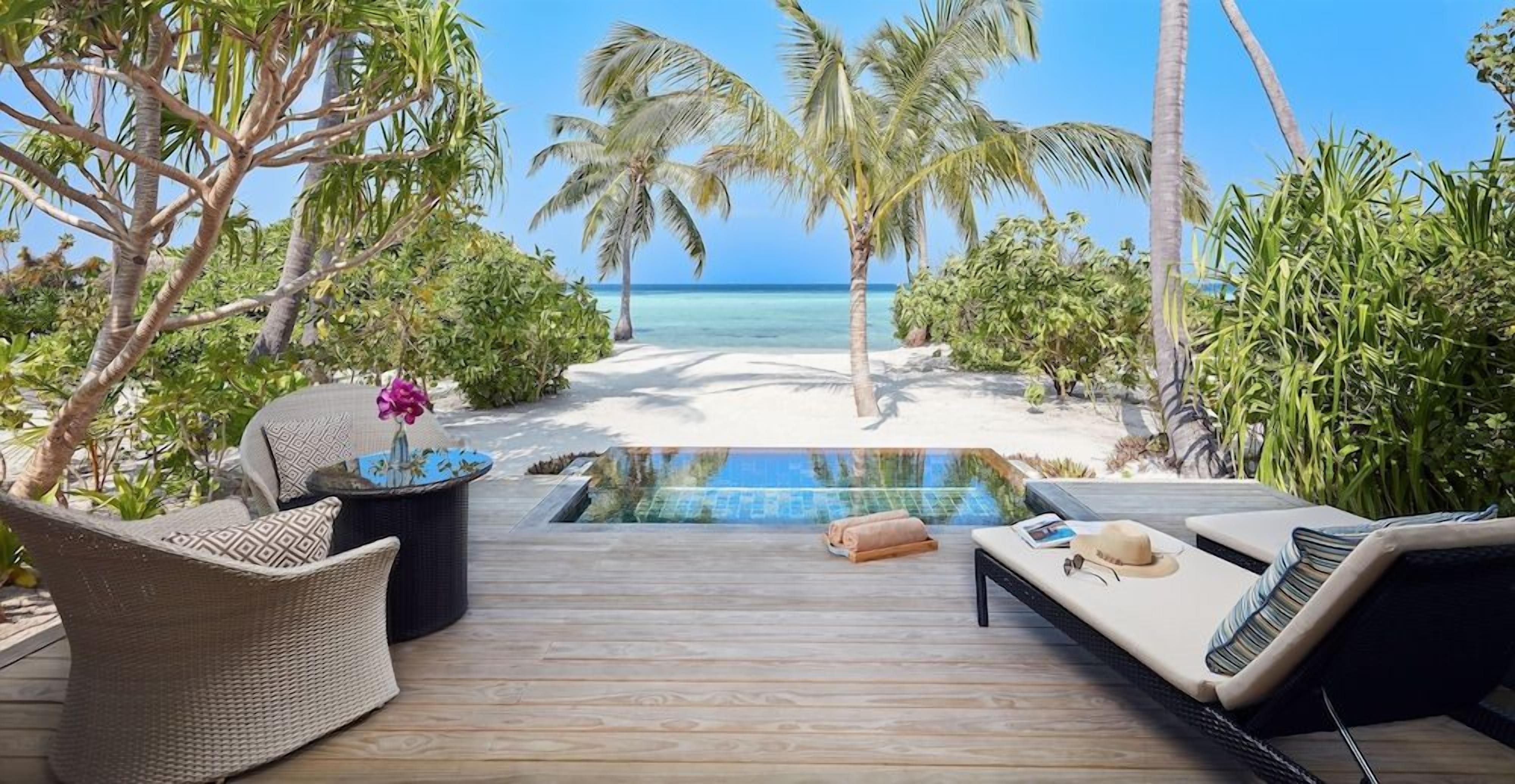 A wooden deck with a pool, lounge chairs, and a view of the beach and ocean.