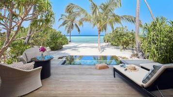 A wooden deck with a pool, lounge chairs, and a view of the beach and ocean.