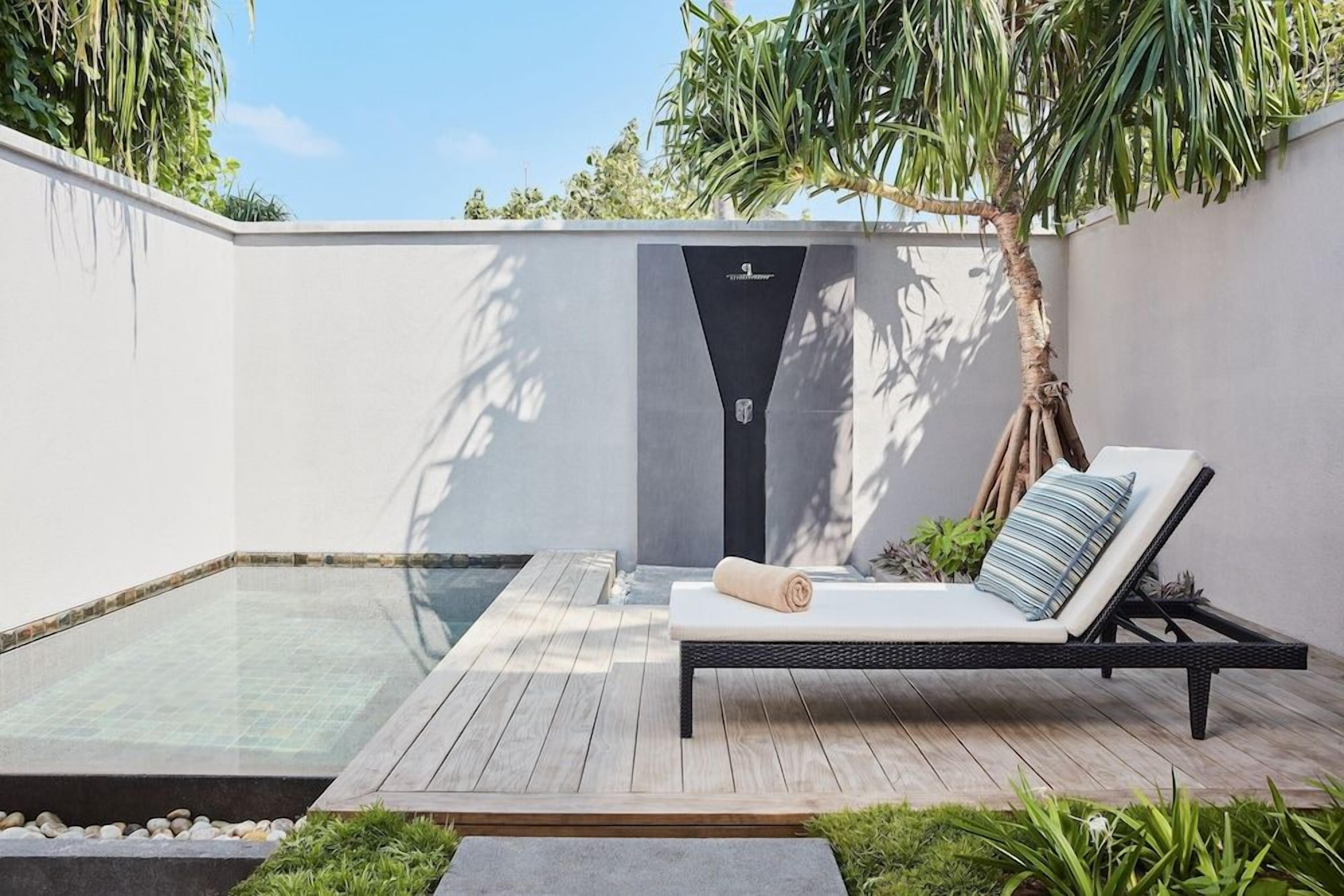 A modern outdoor lounge area with a glass-enclosed pool, a wooden deck, and a black metal lounge chair with cushions.