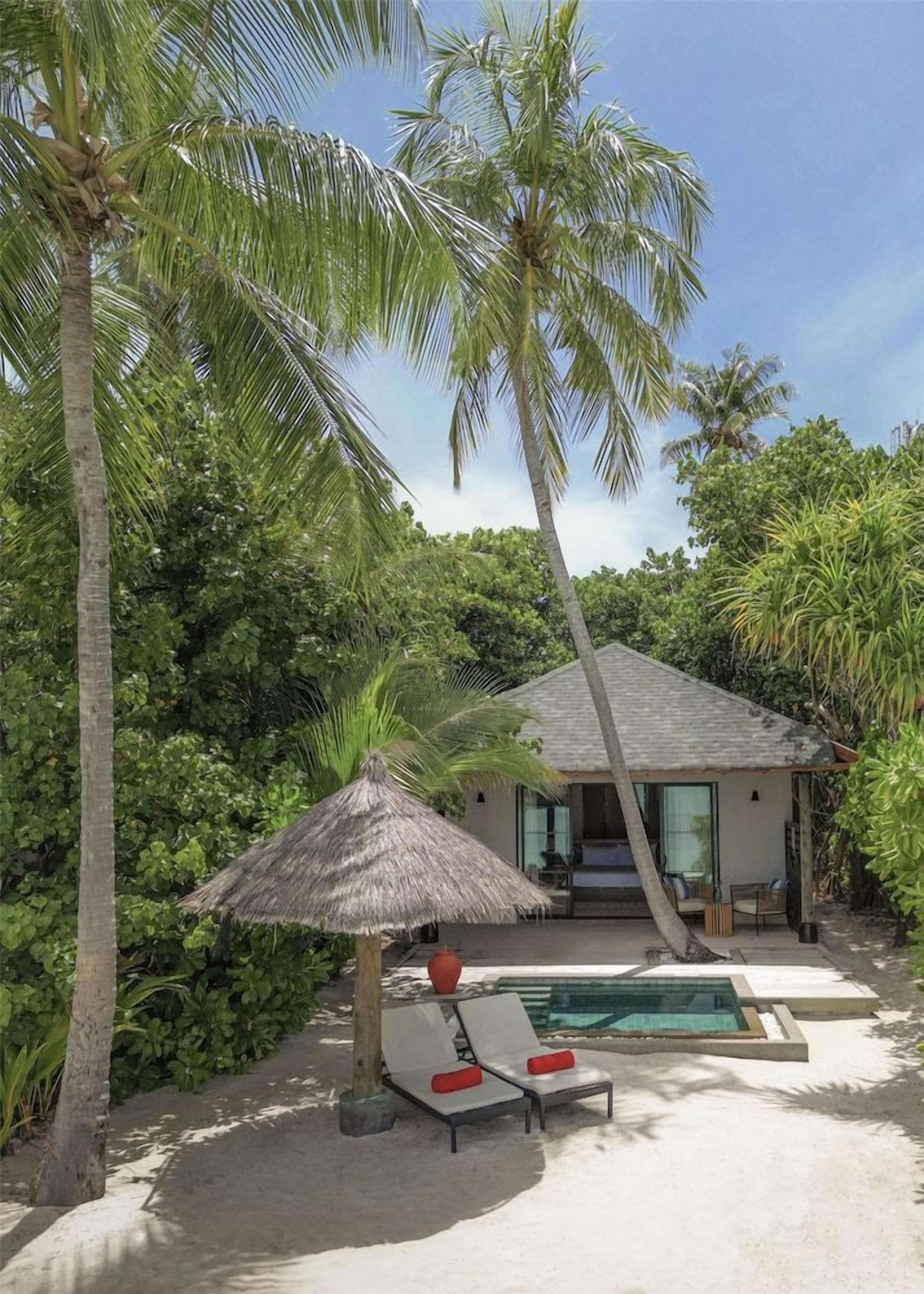 A beachfront property with a pool, lounge chairs, and a thatched-roof structure.