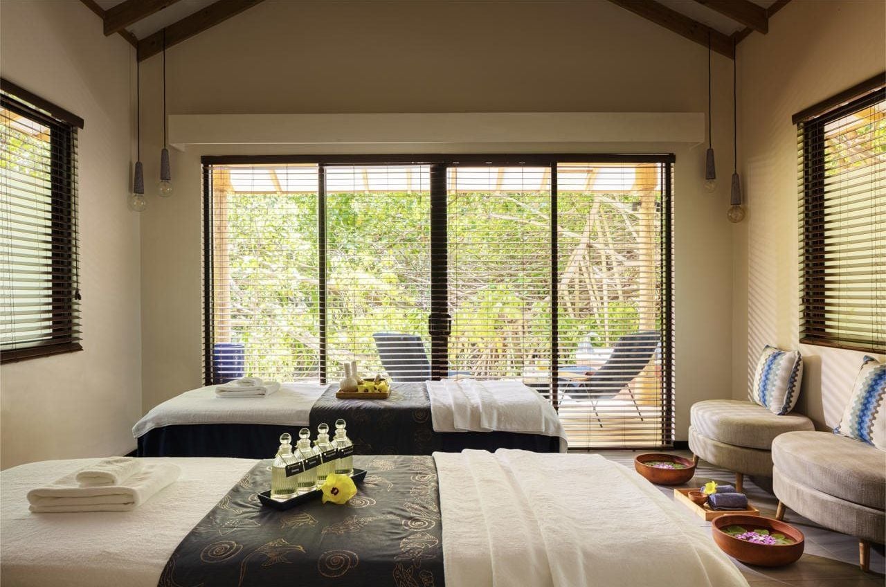 Un cuarto de spa con dos camas, un sofá y vistas a la vegetación a través de amplias ventanas.