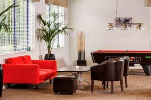 Een pooltafel met rood en zwart tafelkleed, een rode bank, een zwarte fauteuil, een klein tafeltje en een bloempot met plant.