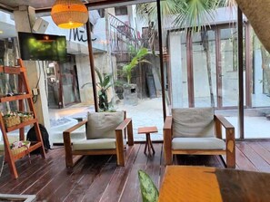 A room with two wooden chairs, a small table, a TV, and a large window overlooking a courtyard with plants and a staircase. - Selina Tulum (Tulum)