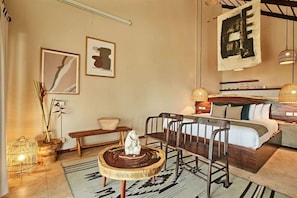 A cozy room with a bed, a wooden bench, a woven stool, and a hanging light fixture. - Selina Tulum (Tulum)