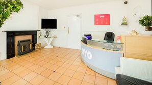 A reception area with a fireplace, a television, a reception desk, and a potted plant. - OYO Marina (Sandown)