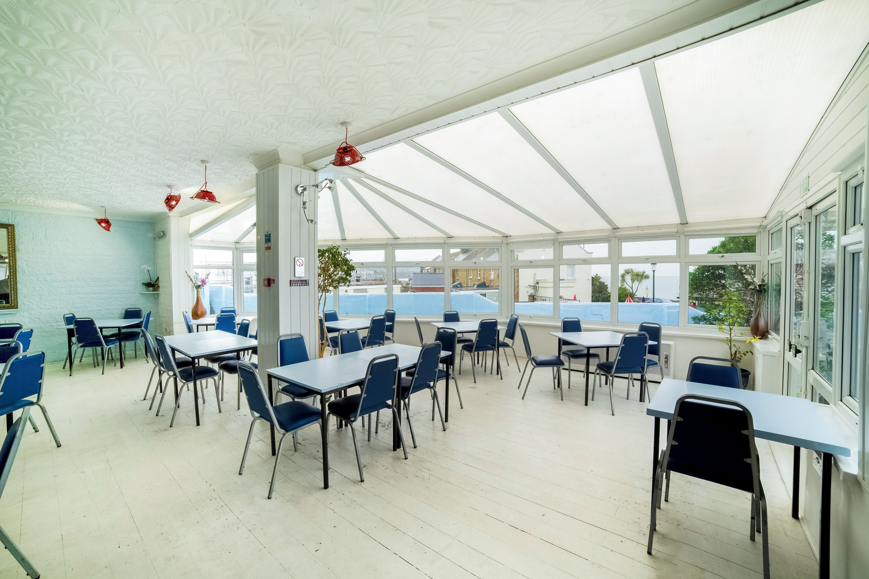 A covered outdoor seating area with tables and chairs, large windows, and a view of the sea.