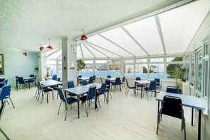 A covered outdoor seating area with tables and chairs, large windows, and a view of the sea. - OYO Marina (Sandown)