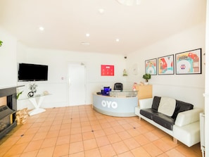 A reception area with a reception desk, a flat-screen TV, a sofa, and a fireplace. - OYO Marina (Sandown)