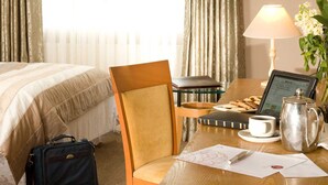 Una habitación de hotel con una cama, un escritorio con una computadora portátil, una lámpara, una cafetera y una silla.