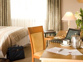 Una habitación de hotel con una cama, un escritorio con una computadora portátil, una lámpara, una cafetera y una silla.