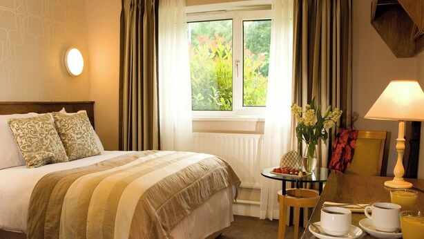 Una habitación de hotel con una cama, una mesa con desayuno, una ventana con cortinas y una lámpara.