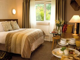 Una habitación de hotel con una cama, una mesa con desayuno, una ventana con cortinas y una lámpara.