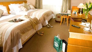 Habitación de hotel con dos camas, una mesita con una lámpara, una silla, un escritorio con una computadora y una ventana con cortinas.