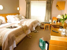 Ett hotellrum med två sängar, ett litet bord med en lampa, en stol, ett skrivbord med en dator och ett fönster med gardiner.