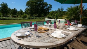 A wooden deck with a dining table set for a meal, overlooking a swimming pool. - Club Royal Océan La Prade by Interhome (Moliets)