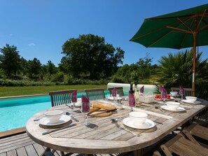 A wooden deck with a dining table set for a meal, overlooking a swimming pool. - Club Royal Océan La Prade by Interhome (Moliets)