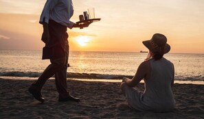 Uma pessoa servindo bebidas numa praia ao pôr do sol.