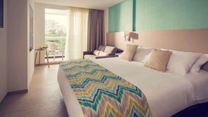 A hotel room with a large bed, a desk with a chair, a sofa, and a view of the outdoors. - Mercure Santa Marta Emile (Santa Marta)