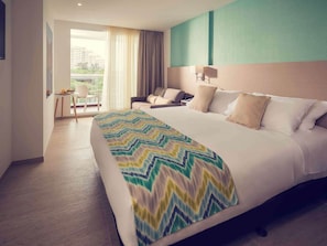 A hotel room with a large bed, a seating area with a chair and table, and a view through a window.
