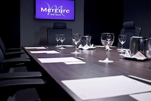 A conference room at Mercure Hotels with a long table set for meetings, chairs, and a television displaying the hotel name.