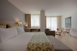 Quarto de hotel com cama, escrivaninha, cadeira, sofá e mesa de jantar com cadeiras.