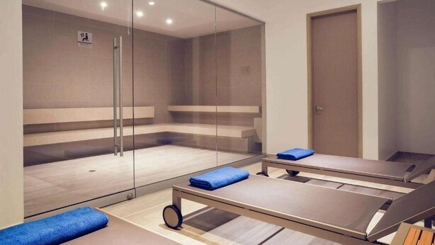 A modern room with a glass partition, a wooden floor, and a blue towel on a massage table. - Mercure Santa Marta Emile (Santa Marta)