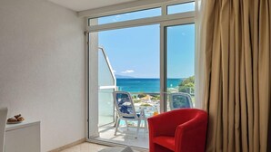 A hotel room with a bed, a red chair, a white desk, and a view of the ocean through a large window. - Maslinica Hedera Hotel (Labin)