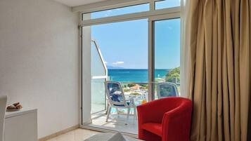 Camera d'albergo con un letto, una poltrona rossa, una scrivania bianca e vista sull'oceano attraverso un'ampia finestra.
