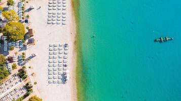 Una vista aerea di una spiaggia con file di lettini e ombrelloni, un mare cristallino e una piccola barca all'orizzonte.
