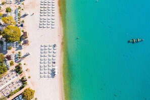 Vista aérea de una playa con filas de tumbonas y sombrillas, un mar azul cristalino y un pequeño barco a lo lejos.