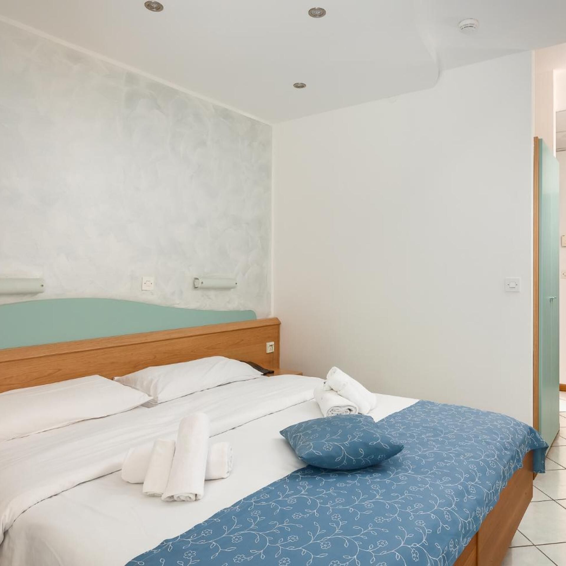 A bedroom with a bed, pillows, and a wall-mounted light fixture.