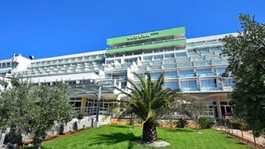 A modern hotel with a green and white facade, multiple balconies, and a well-maintained garden with palm trees. - Maslinica Hedera Hotel (Labin)