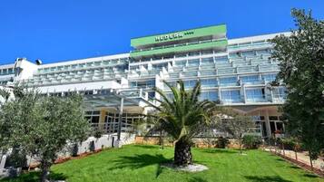 Un hotel moderno con facciata verde e bianca, numerosi balconi e un giardino curato con palme.