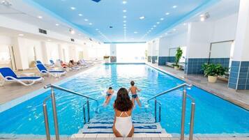 Una piscina interna con pareti in piastrelle blu, una scala per la piscina e lettini da relax lungo i bordi.