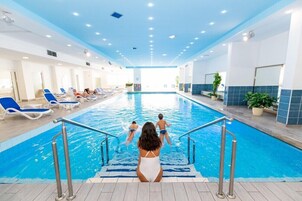 Piscina interna com paredes azulejadas em azul, escada de acesso e espreguiçadeiras nas laterais.