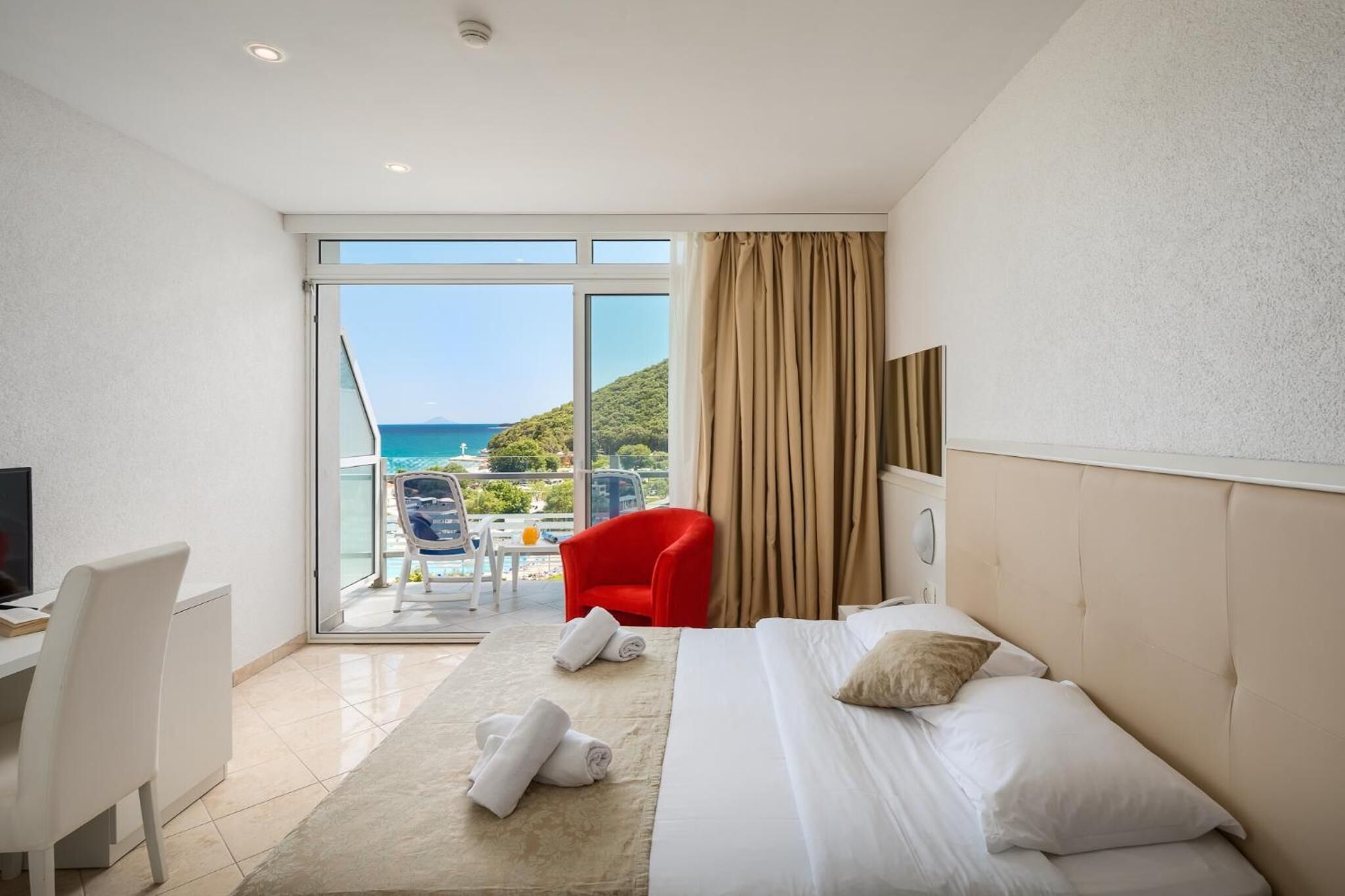 A hotel room with a bed, a desk, a chair, and a view of the sea.