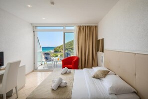 A hotel room with a bed, a desk, a chair, and a view of the sea. - Maslinica Hedera Hotel (Labin)