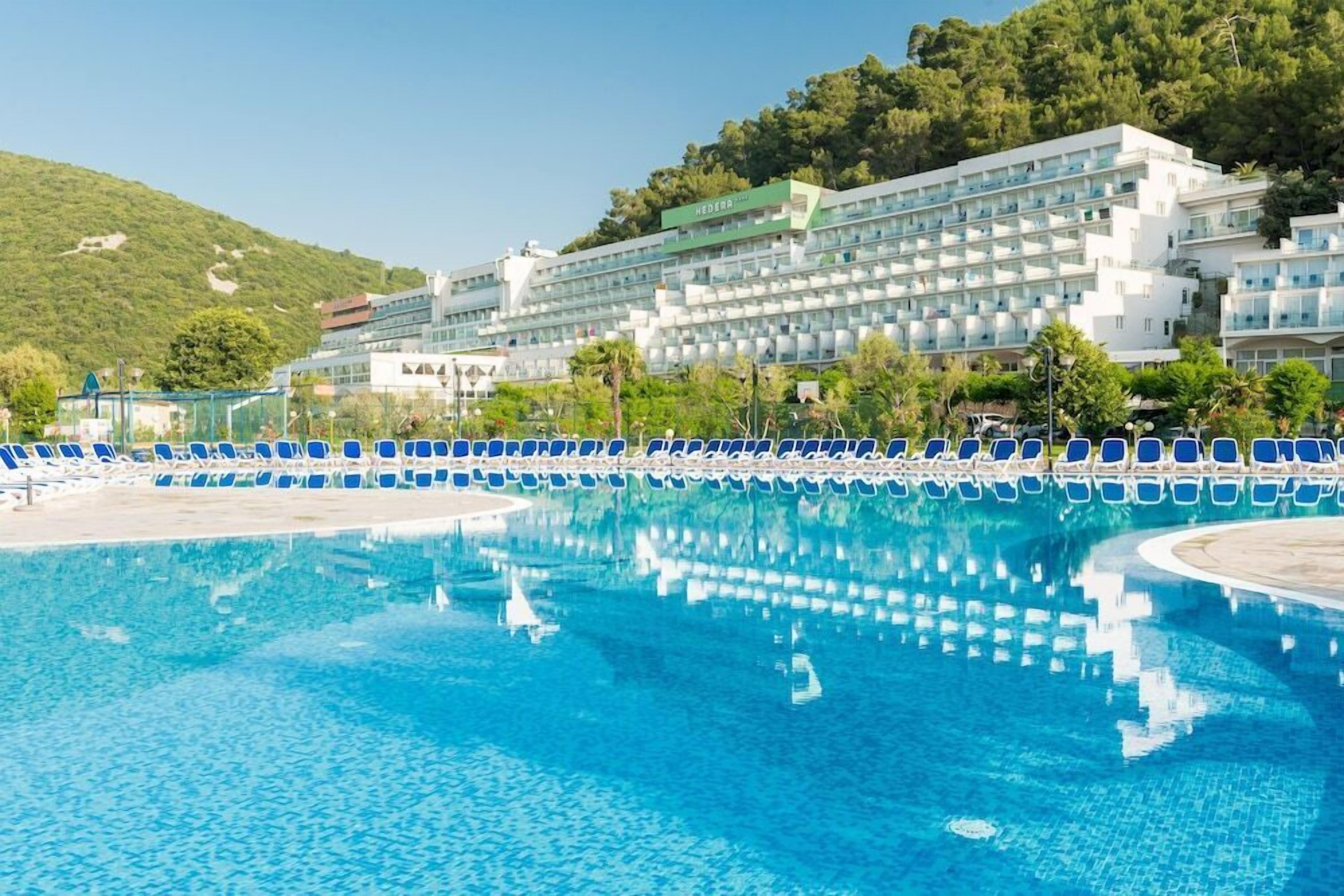 Ett hotell med en swimmingpool, en stor byggnad med flera våningar och ett kuperat landskap i bakgrunden.