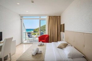 Camera d'albergo con un letto, una scrivania, una sedia, una TV e vista sul mare.