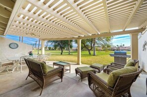 Eine Terrasse im Freien mit Korbmöbeln, einem Grill und Blick auf eine Rasenfläche.