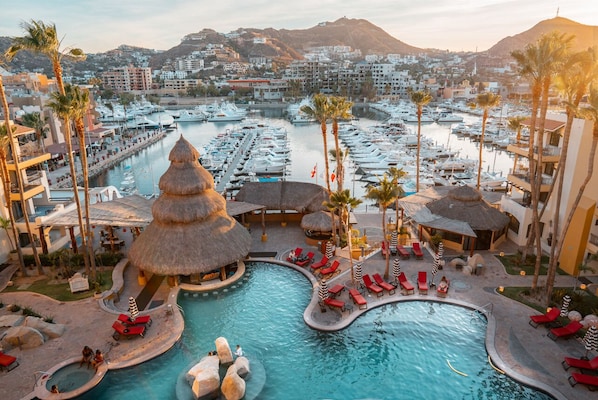 A resort with a large pool, palm trees, and a marina in the background.
