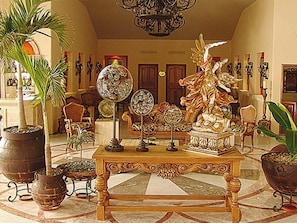 Un hall d’entrée avec une grande table richement décorée, des plantes en pot et une statue.