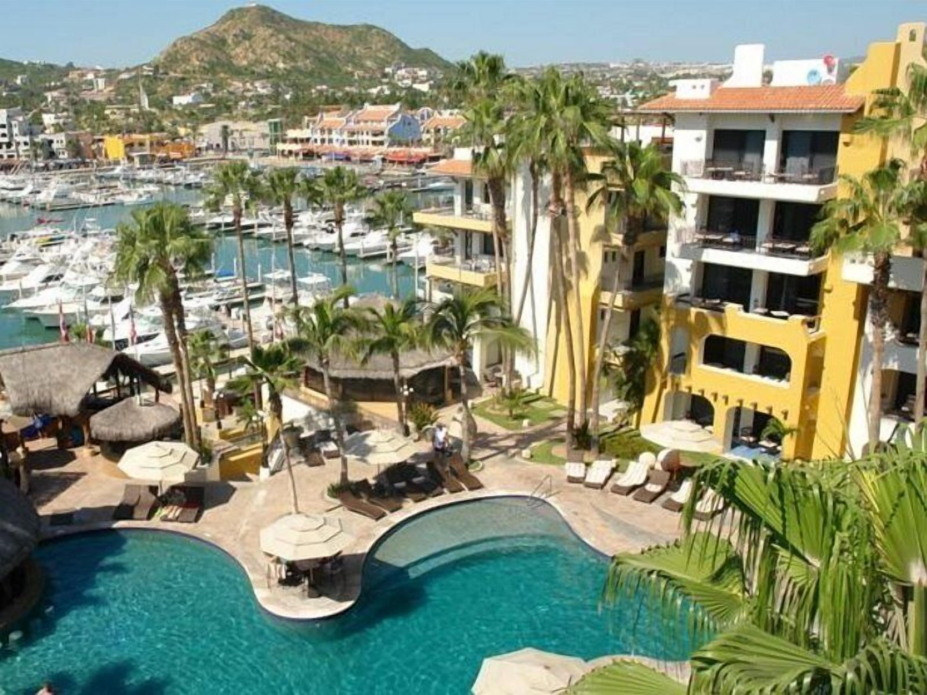 A marina with boats, a pool with lounge chairs, and a building with balconies.
