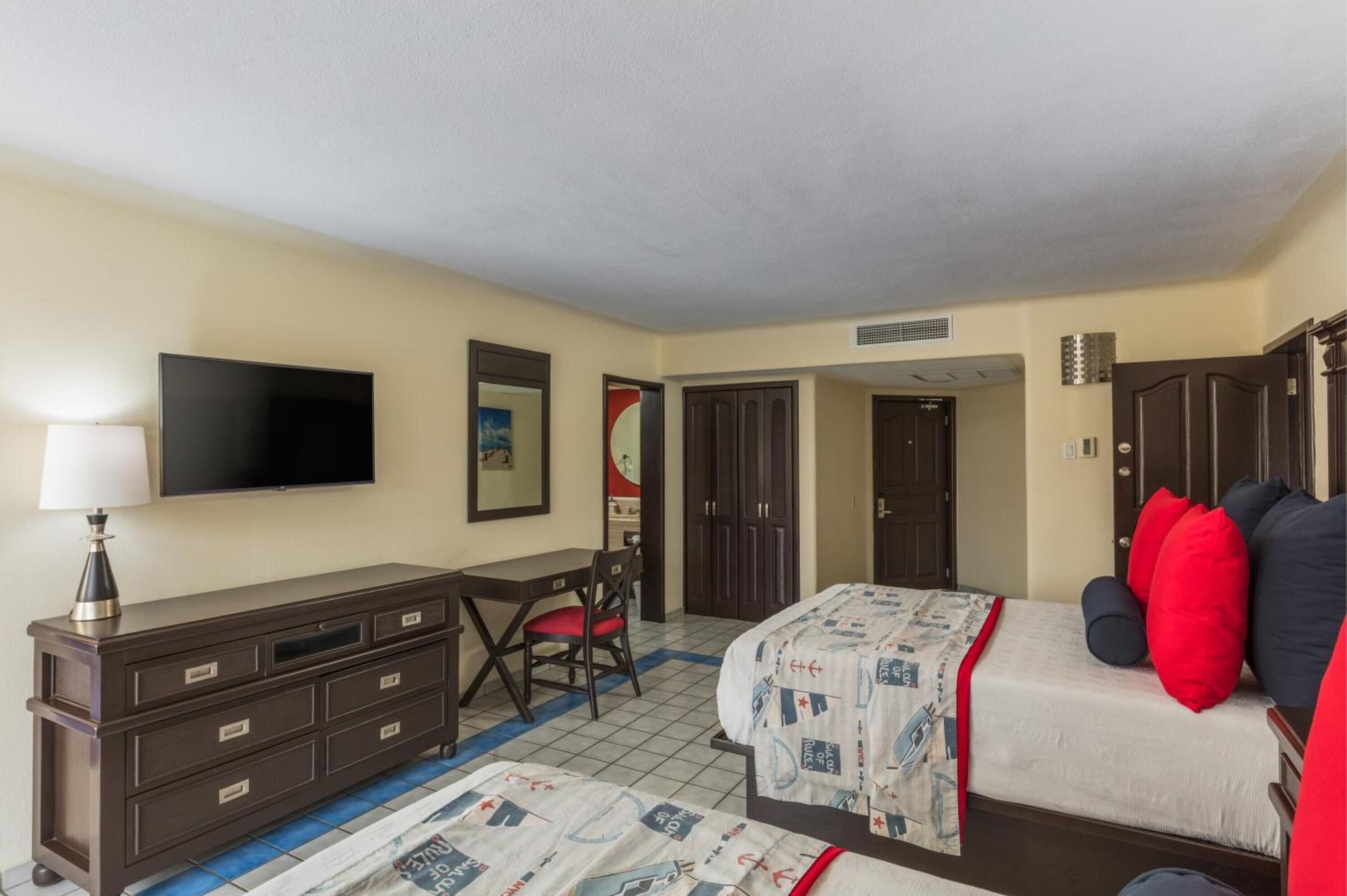 A hotel room with a bed, a desk, a chair, a TV, and a wardrobe.
