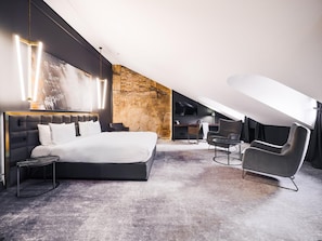 Un dormitorio moderno con una cama grande, un escritorio y una silla, que presenta una pared de piedra y un techo inclinado.