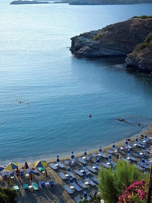 A beach with sun loungers and umbrellas, a rocky coastline, and calm sea.