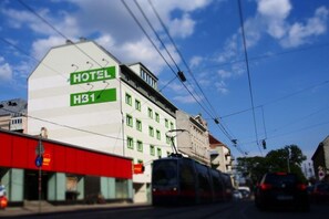Ein Hotel mit einem Schild, das 'HOTEL H31' anzeigt, und einer Straßenbahn im Vordergrund.