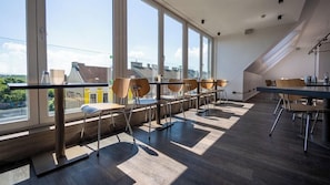 A modern hotel room with large windows, a dining area with chairs and tables, and a view of buildings outside. - Smart Hotel Schonbrunn (Vienna)