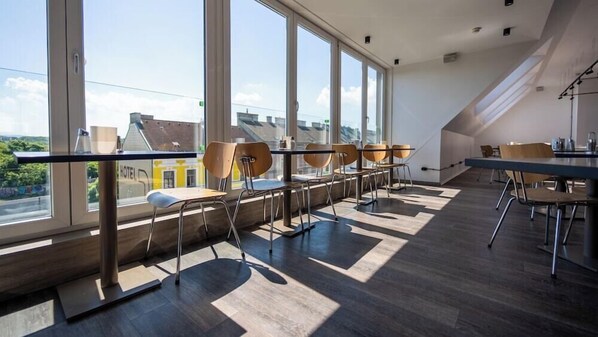 A modern hotel room with large windows, a dining area with chairs and tables, and a view of buildings outside. - Smart Hotel Schonbrunn (Vienna)