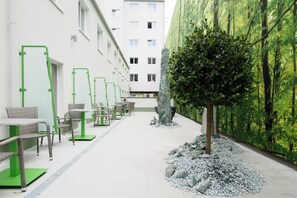 A corridor with outdoor seating, a tree, and a building with windows. - Smart Hotel Schonbrunn (Vienna)